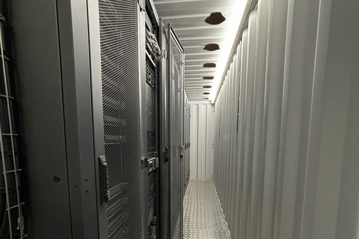 An aisle between two rows of racks, perforated doors, green status lights inside.